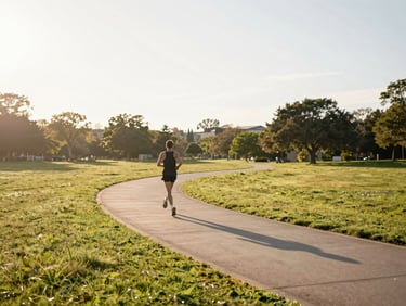 Wide shot of a runner's path winding through a park at golden hour, soft warm tones, low horizon