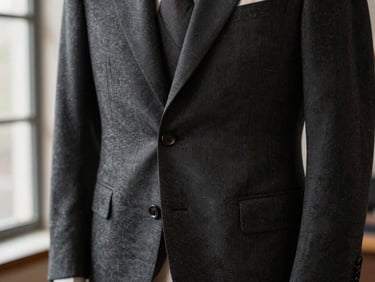 Close-up of a charcoal bespoke suit jacket hanging in a softly lit atelier, showcasing hand-padded canvas structure