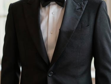 Detail shot of a black tuxedo jacket lapel with silk facings and horn buttons, moody shadows