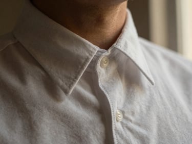 Macro shot of a crisp white cotton shirt collar with hand-rolled buttonholes, warm side-lighting