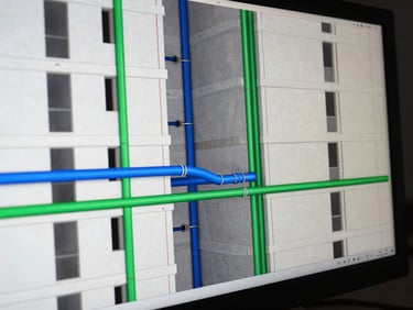 Close-up of a BIM coordination model on a monitor, showing a residential tower floor plate with electrical conduits in blue and hydraulic pipes in green intersecting at a corridor junction, high-contrast studio lighting, no text overlays