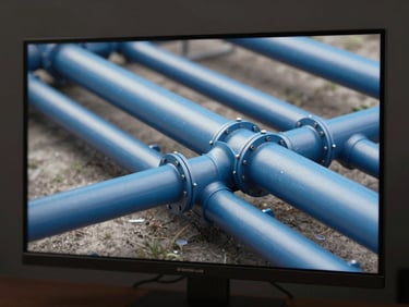 Close-up BIM model of hydraulic piping network — water supply and drainage pipes in blue tones — rendered on monitor screen, studio strobe lighting, dark neutral background, technical precision framing