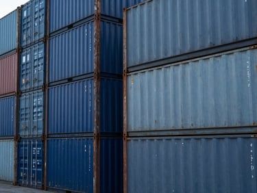 Close-up of industrial steel containers stacked at a busy port terminal, sharp focus, metallic textures, cool blue daylight