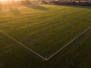 Sunlit, expansive plot of land with clear boundary markers, golden hour light, wide-angle drone shot