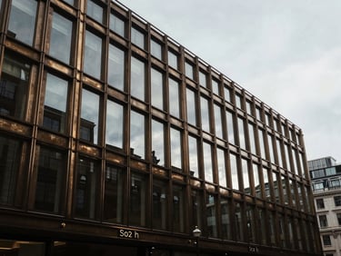 Tight crop of a bronze and glass commercial facade in the City of London, moody late afternoon light, desaturated tones