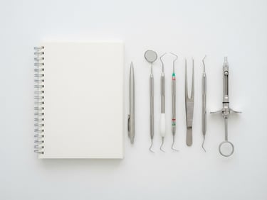 A minimalist flat-lay of modern dental tools and a clean notebook on a sterile white surface under high-key clinical daylight, 50mm lens