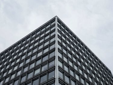 Low-angle architectural crop of a structured steel and glass building corner against a stark overcast sky.