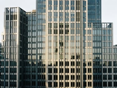 Wide architectural shot of a modern financial district building facade, sharp directional window light, desaturated slate and cream tones, high contrast, 35mm lens
