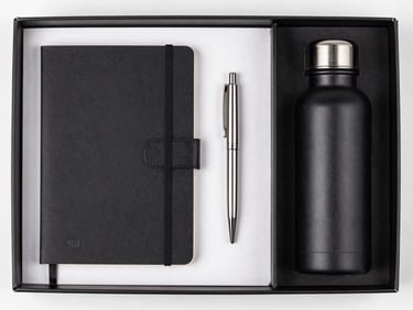 Top-down flat lay of a premium corporate onboarding kit, including a black notebook, a metal pen, and a sleek water bottle, all neatly arranged in a textured box with crisp branding