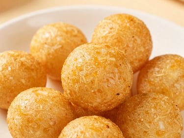 Golden cheese balls stacked on a white plate, soft warm lighting, macro food photography