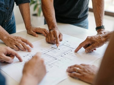 Close-up of diverse hands collaborating around a blueprint or document on a table, community leaders discussing plans, natural daylight, warm organic tones, documentary film photography.