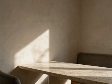 Architectural detail of a quiet lounge featuring raked plaster walls, a low travertine table, and soft shadows cast by indirect morning light.