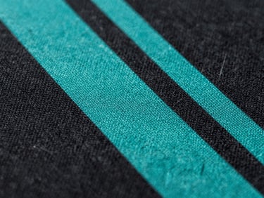 Macro close-up of a high-density electric teal screen print on heavy black cotton fabric, showing detailed fiber weave and sharp vector edges.