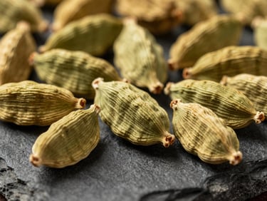 Macro close-up of whole dried cardamom pods and premium spices on a dark stone surface, warm gold lighting