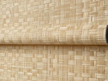 Close-up detail shot of woven roller blind fabric texture, soft north-facing daylight catching the weave pattern, warm cream and sand tones, no people, tight macro framing showing individual fabric threads and the way light filters through the material, landscape aspect