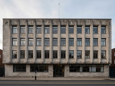 Wide architectural frame of a mid-century civic building facade in overcast afternoon light, stone or concrete exterior, street level visible below, minimal pedestrians — used as a country intelligence visual anchor, no flags or landmarks