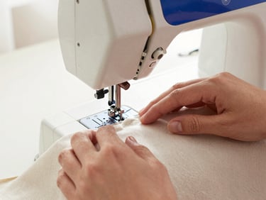 Hands gently guiding a piece of premium linen fabric through a classic sewing machine, warm natural light, focus on textures