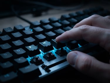 Close-up macro shot of mechanical keyboard switches, fingers positioned on home-row tactile bumps, low-key studio lighting with sharp neon blue accent glow reflecting off keycaps, shallow depth of field.