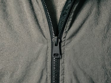 Extreme close-up of a matte black metal zipper on a heavy cotton jacket, stark studio strobe lighting, desaturated concrete background.