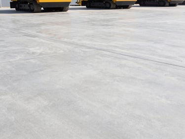 Wide-angle industrial flooring shot with heavy machinery, smooth concrete surface, bright daylight