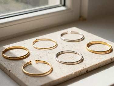 Warm side-lit window sun illuminating a flat lay of gold and silver bracelets on textured stone slabs, minimal styling, 35mm lens