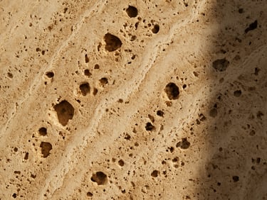 Extreme close-up of raw travertine stone texture, showing deep cream veins and porous cavities under bright sunlight.