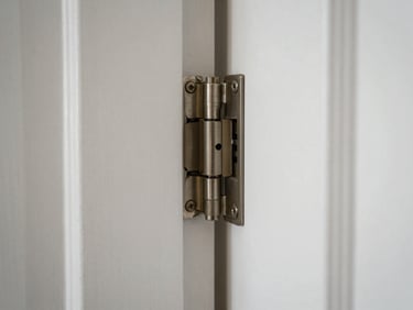 Close-up natural daylight shot, interior — a door hinge freshly re-seated, screws flush, paint edge clean, no people, tight detail framing against white wall