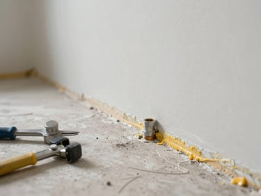Wide natural daylight shot — a utility room showing a sealed pipe joint and freshly caulked skirting, tools resting on the floor beside finished work, no people, clean finish visible