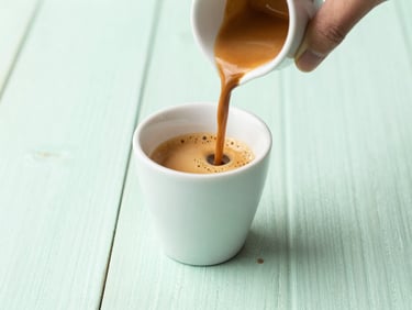 A perfectly poured double shot of espresso in a ceramic cup on a mint green wooden table, bright soft daylight