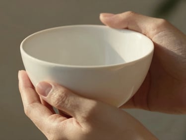 Extreme close-up of delicate hands holding a minimalist ceramic object in warm morning light, soft shadows, luxury feel