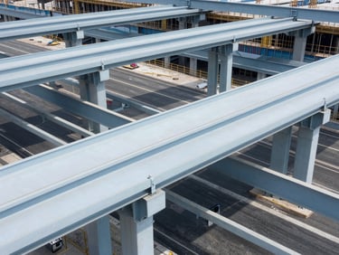 High-angle architectural photograph of a major highway interchange under construction, steel girders, clean blue tones, bright daylight