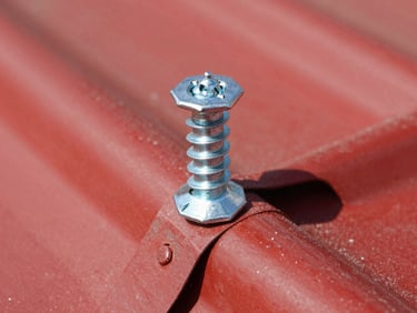 Close-up of a heavy-duty roofing screw with washer securing a red corrugated metal sheet, sharp focus on structural connection