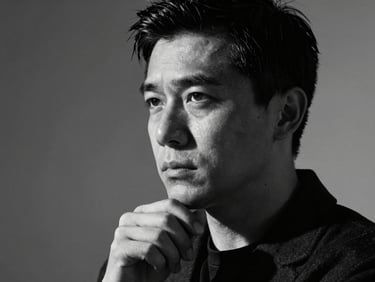 Stylized black and white studio portrait of a male strategist, thoughtful expression, high-contrast studio lighting, deep shadows, 35mm anamorphic lens.