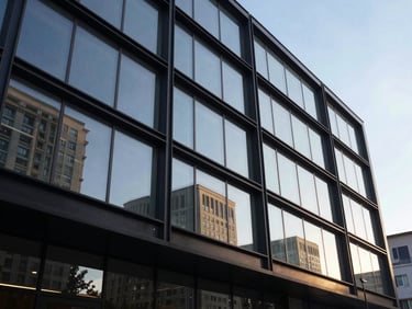 Low-angle morning sun hitting a commercial facade of blackened steel and massive glass spans, reflecting the surrounding urban landscape.