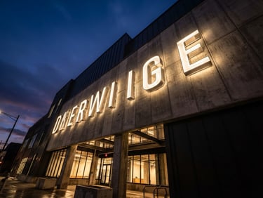 Low-angle architectural shot of massive illuminated channel letters on a modern concrete building facade at dusk, industrial architectural photography