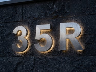 Close-up of brushed stainless steel channel letters with halo backlighting on a dark stone wall, dusk lighting