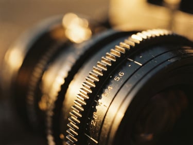 Extreme close-up of a high-end cinema camera lens dial, golden hour light catching the metallic ridges, shallow depth of field, 35mm film aesthetic.