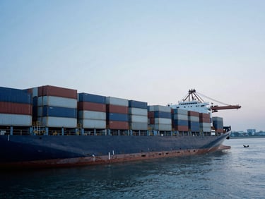 Wide-angle industrial port at dawn, cold steel cargo containers stacked precisely, container ship docked in deep water, desaturated blue tones, 35mm.