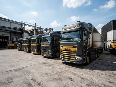 Low-angle heroic shot of a modern transport fleet parked in a high-contrast industrial yard under crisp daylight, sharp industrial photography.
