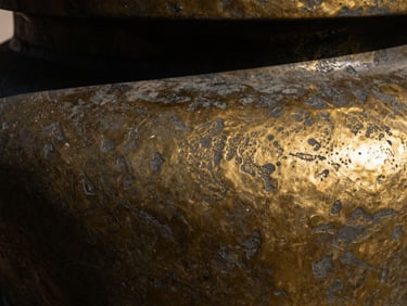 Macro detail of textured cast bronze surface, showing dark gold and black oxidized metallic grain with deep shadows