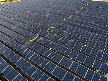 Wide aerial drone shot of massive solar fields stretching to the horizon, sharp midday lighting, deep slate tones