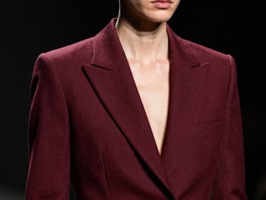 High-contrast editorial close-up of a fashion model in a structured burgundy blazer, dramatic studio lighting, sharp focus, 35mm