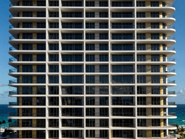 Modern luxury condominium facade with ocean view, sharp coastal sunlight, Hallandale Beach, high contrast.
