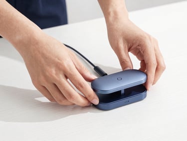 Close-up of hands placing a sleek magnetic cable organizer onto a clean white wooden desk, studio lighting, modern tech aesthetic