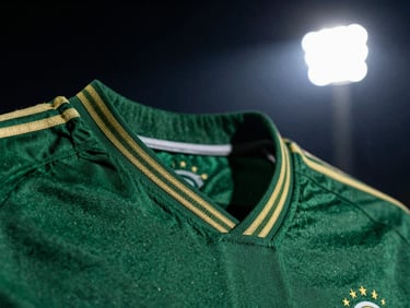 Close-up of a dark green football kit collar with fine gold embroidery, dramatic side lighting, high-contrast.