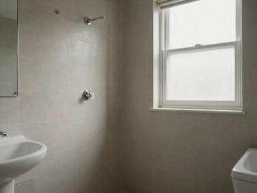 Apartment bathroom with neutral tiles, wall-mounted fixtures, natural light from frosted window, clean and unoccupied, honest listing photo