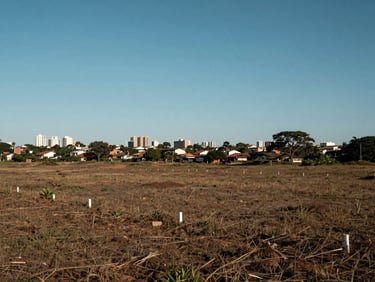 Open land plot in a Brazilian urban fringe neighborhood, clear sky, distant city reference visible at horizon, flat ground with visible boundary markers
