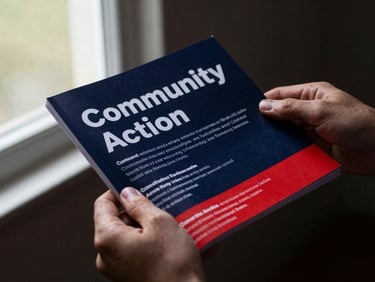 Dynamic close-up shot of hands holding a printed community action guide, soft natural window light, 35mm.