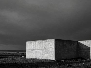 Stark black and white landscape of a lone concrete structure against a heavy, dark overcast sky, high-contrast side lighting, visible film grain, medium-format 80mm lens composition