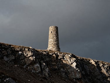 Stark, high-contrast landscape of a solitary stone tower on a barren cliffside under a heavy, overcast sky, dramatic side lighting, medium-format film grain.